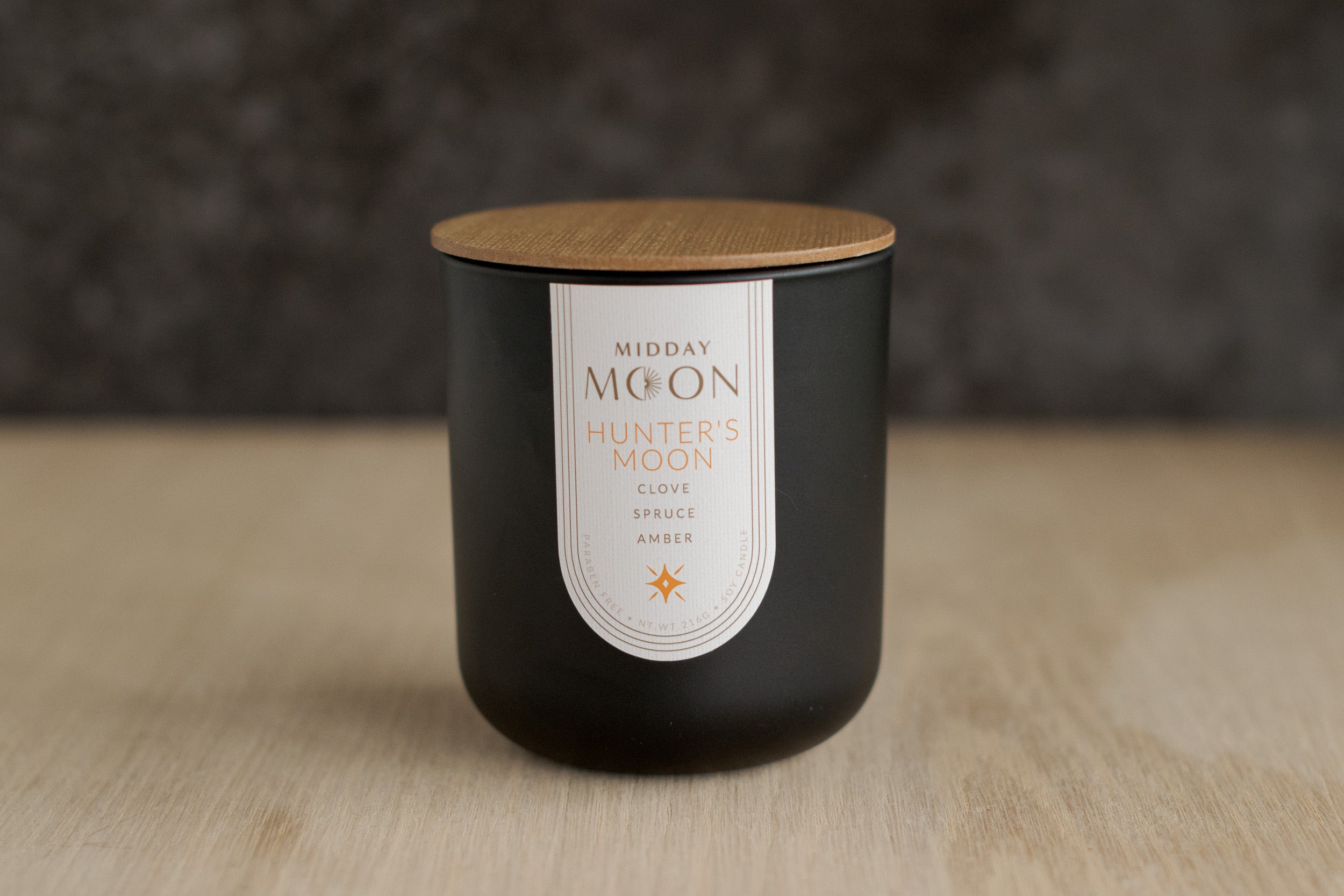 clove, spruce, and amber scented candle in a black jar displayed on a wooden surface.