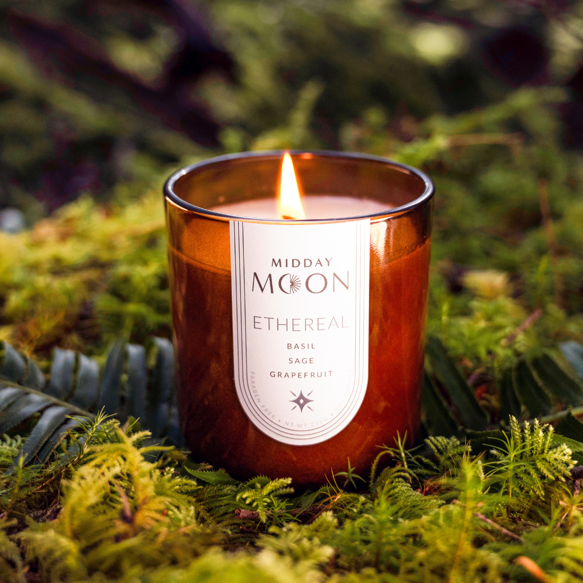 Scented soy candle on a bed of moss in a lush forest setting. Basil, sage, and grapefruit scented candle.
