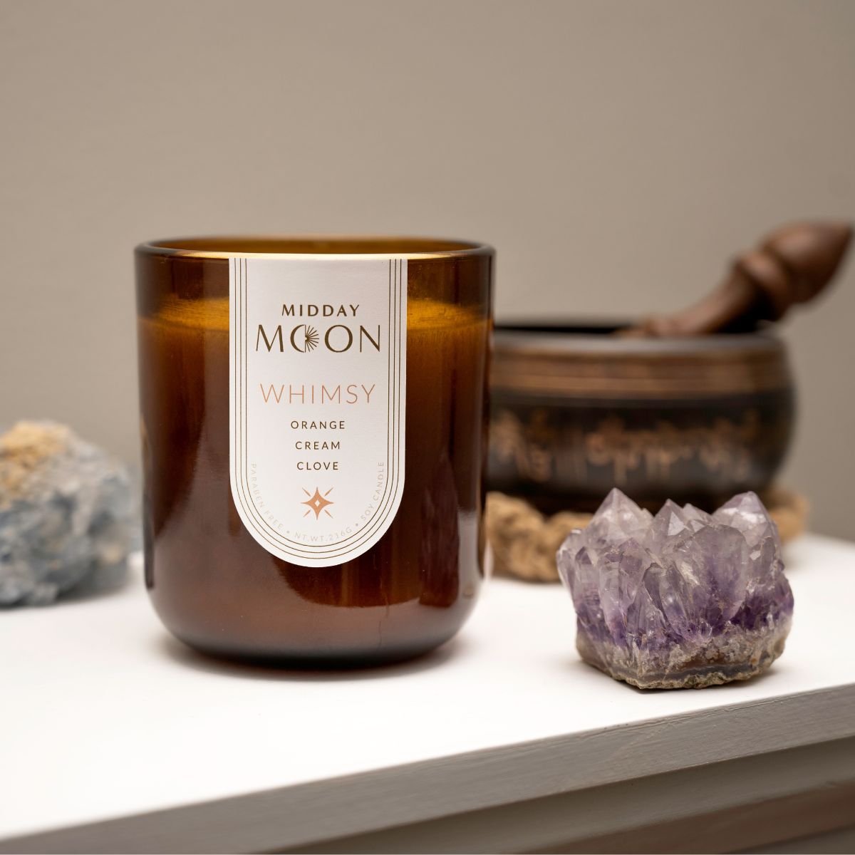 orange scented candle in an amber jar. Midday moon soy candle staged with amethyst crystals