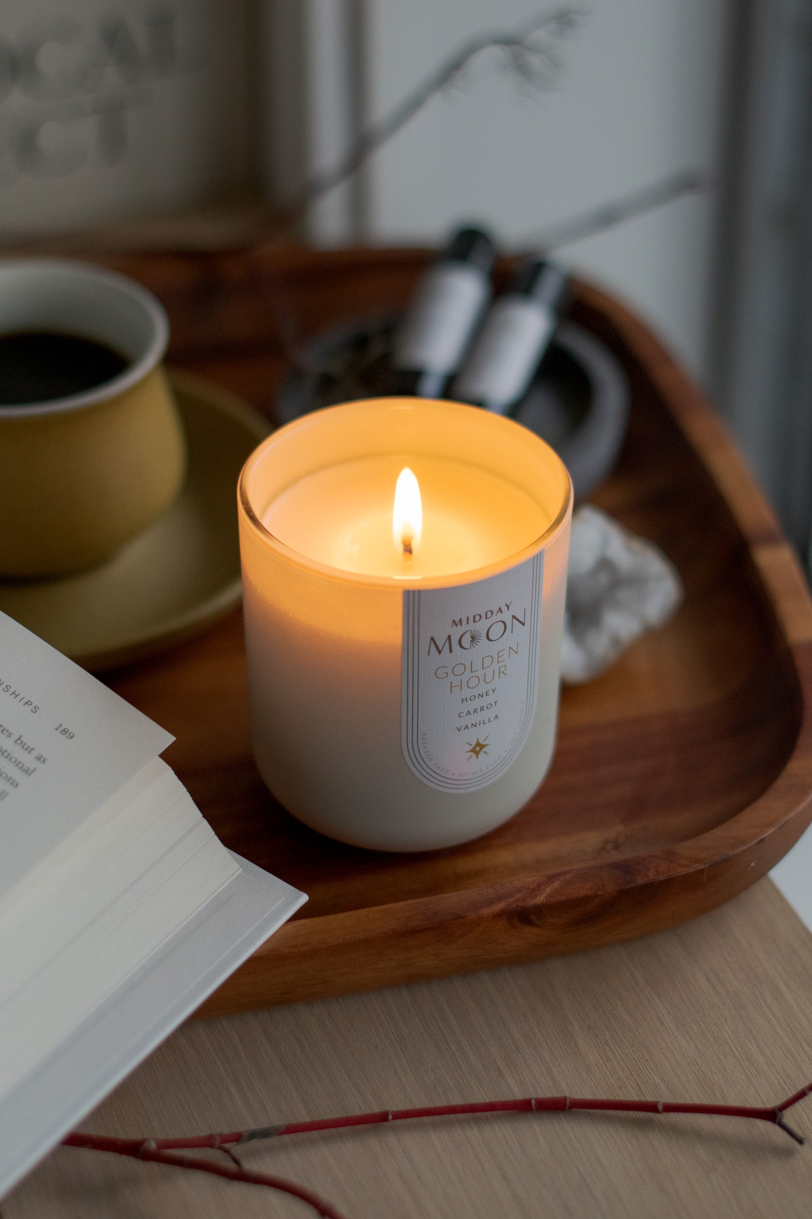 a lit candle displayed on a wooden tray with a book and cup of tea.